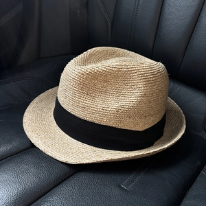 Detail of light brown straw fedora with black ribbon on a black leather surface