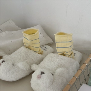 Detail of plush white bear slippers with soft morandi striped socks for cozy home comfort