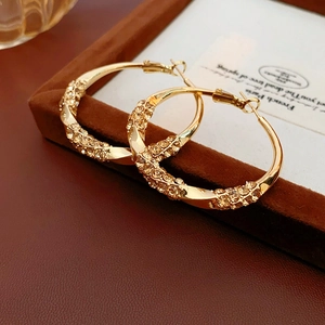 Macro shot of twisted gold hoop earrings with sparkling crystals on a brown velvet box