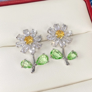 Macro view of crystal daisy earrings with yellow center and green leaves in a jewelry box