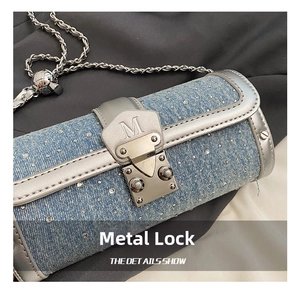 Close-up of silver metal clasp with M engraving on light blue denim cylinder bag
