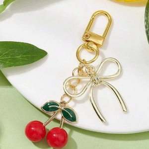 Shiny red cherry keychain with gold bow and green leaves on a white ceramic plate