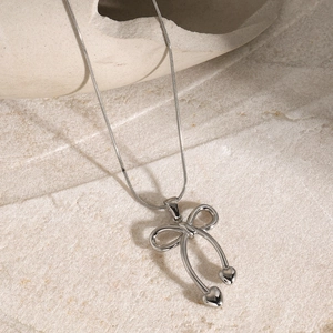 Detailed view of silver bow necklace with heart charms on textured stone surface