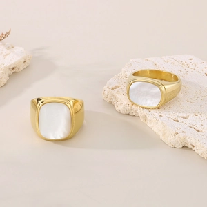 Close-up of two golden stainless steel rings with white shell inlays on stone base
