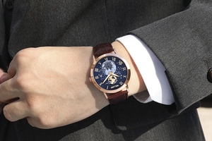 Detail of rose gold men's watch with blue map dial and brown leather strap on wrist