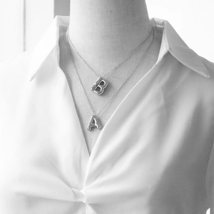 Silver bubble letter A and B pendant necklaces layered on minimalist cross chains