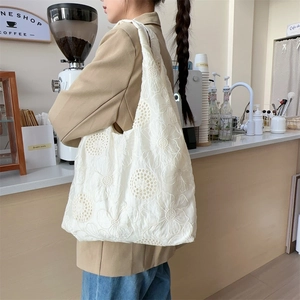 Close-up of white daisy embroidery and hollow-out texture on canvas tote bag
