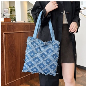 Detail of blue denim tote bag featuring quilted star patterns and distressed frayed edges