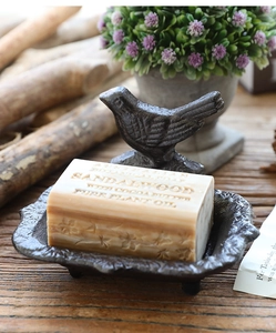Detail of vintage cast iron bird soap dish holding a sandalwood bar on rustic wood