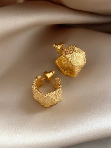 Macro shot of gold wide C-shaped earrings with hammered texture on champagne satin fabric