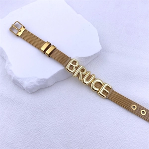 Close-up of gold mesh bracelet with BRUCE letter beads on white plaster block