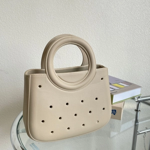 Détail du sac de plage EVA beige clair avec découpes rondes sur une table en verre
