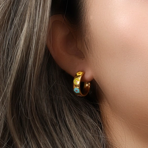 Close-up of golden hoop earrings with colorful enamel floral patterns on a model