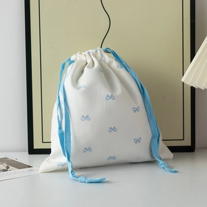 Detail of white cotton drawstring bag with blue ribbon bows and herringbone straps