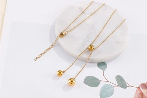 Detail of a gold stainless steel beaded necklace on a marble coaster with eucalyptus decoration