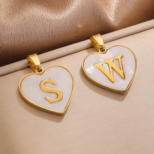 Macro shot of gold heart pendants with white pearl inlay and engraved letters S and W
