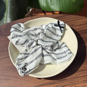Polyester scrunchie with musical notes pattern and black bow in a ceramic dish