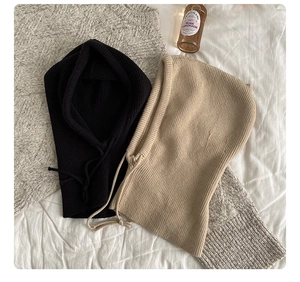 Flat lay of black and beige knitted balaclava hats with drawstring on white sheets