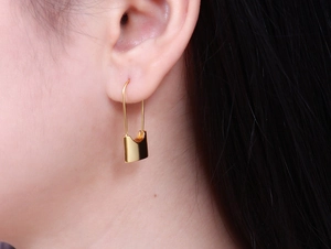 Detail of 18k gold plated safety pin lock earrings worn on ear with polished finish