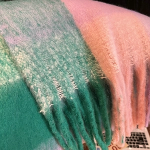 Macro shot of thick knit rainbow checkered scarf showing pastel green and pink tassels