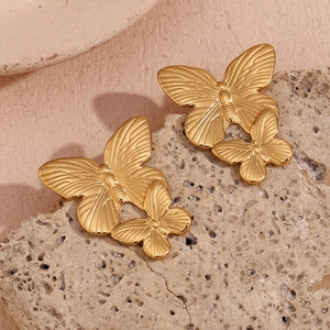 Detail of overlapping gold butterfly earrings on a natural light stone background