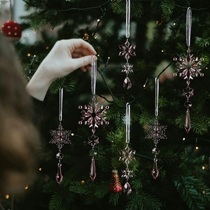 Close-up of pink acrylic snowflake hanging on a Christmas tree with festive lighting