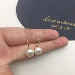 Detail of high-luster freshwater pearl earrings held by hand to show size and golden hooks
