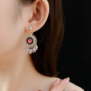 Close-up of model wearing ethnic style gold earrings with pink gemstone and purple tassels