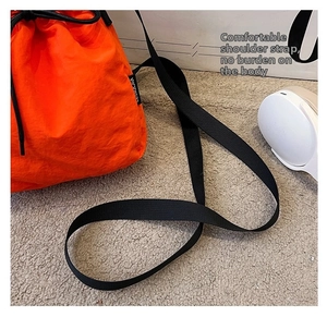 Detail of a bright orange drawstring bucket bag with durable black nylon shoulder straps