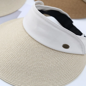 Close-up of a straw sun hat featuring a wide brim and a metallic brand logo plaque