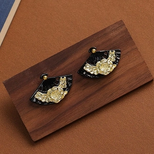 Detail of Chinese fan-shaped earrings with gold floral relief on black metal surface