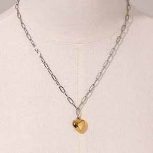 Detail of two-tone gold heart pendant with silver paperclip chain on a beige mannequin