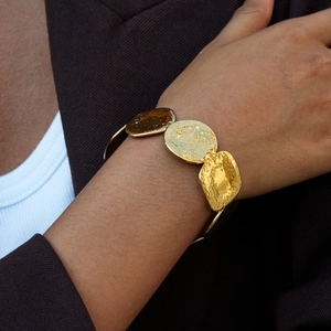 Close-up of golden hammered disc bangle on model's wrist with elegant brown suit