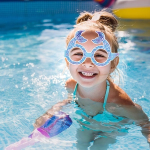 Blue mermaid paper glasses for kids' party worn by a girl smiling in a bright pool