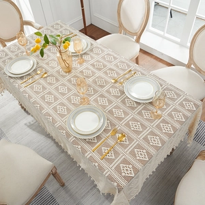 Elegant beige lace tablecloth with hollow patterns and fringe edges on a dining table