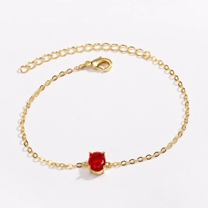 Detail view of a gold-plated bracelet with a red oval gemstone and lobster clasp closure