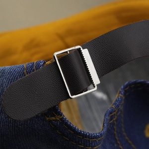 Détail macro du bracelet en cuir marron et boucle argentée sur casquette en jean