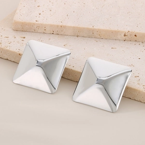 Detail of silver square pyramid stud earrings on textured beige stone surface