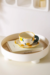 Macro detail of hand-painted ceramic lemon pattern teacup and saucer set on wooden tray