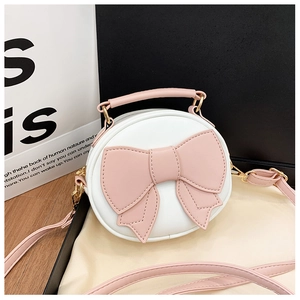 Detail of round white kid purse featuring a pink leather bow and golden hardware