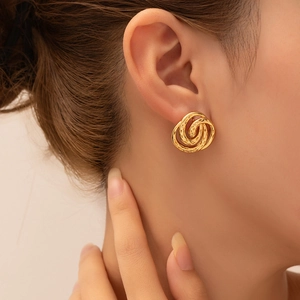 Detail of twisted gold flower earrings with vintage texture on a model's ear