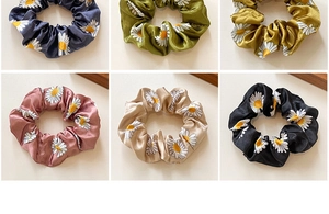 Detail showing various colors of satin daisy scrunchies with smooth texture and soft sheen