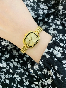 Close-up of gold square dial watch with metal mesh strap worn on elegant wrist