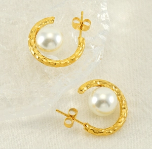 Detail of gold-plated hammered C-shape earrings featuring a large glossy white pearl