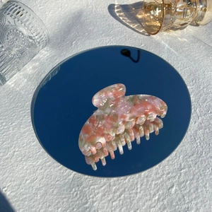 Close-up of a marble acetate claw clip in pink and green on a reflective mirror base