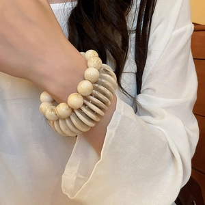 Detail of stacked acrylic beaded bracelets with cream marble texture on a model wrist