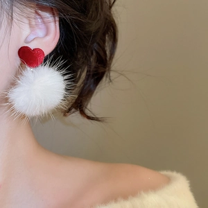 Gros plan de boucles d'oreilles cœur rouge et pompon blanc portées par un mannequin