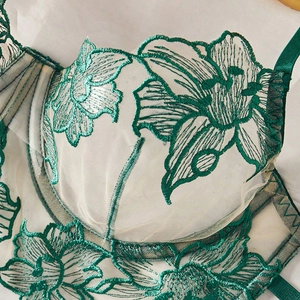 Close-up of deep green floral embroidery on sheer mesh fabric with satin strap details