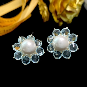 Macro shot of blue crystal flower earrings with a white pearl center on black background