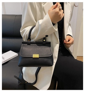 Détail du sac à main noir à texture litchi avec fermoir doré porté par un mannequin